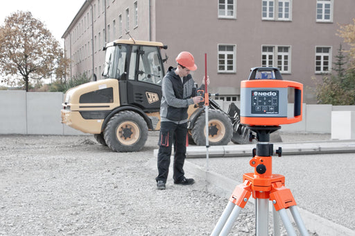 Nedo Heavy-Duty Elevating Tripod supporting a laser level, worker adjusting measuring rod on construction site.