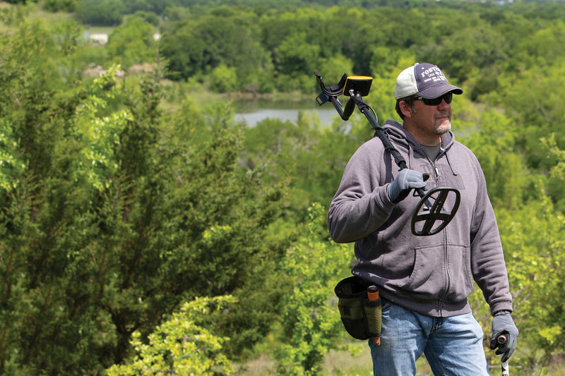 Detectorist carrying a Garrett ACE Apex metal detector across an open field